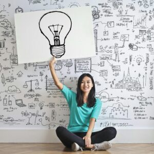 Young woman holds a light bulb drawing against a creative brainstorming wall.